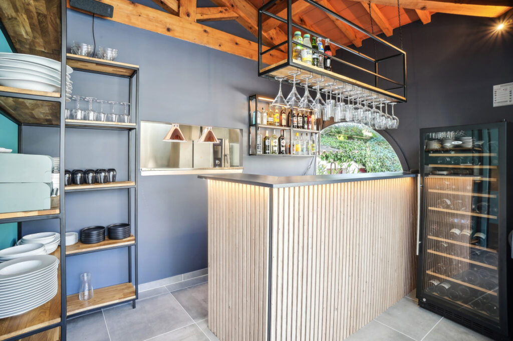 Bar intérieur moderne avec comptoir en bois, cave à vin vitrée et rangements design dans un établissement premium à Sommières